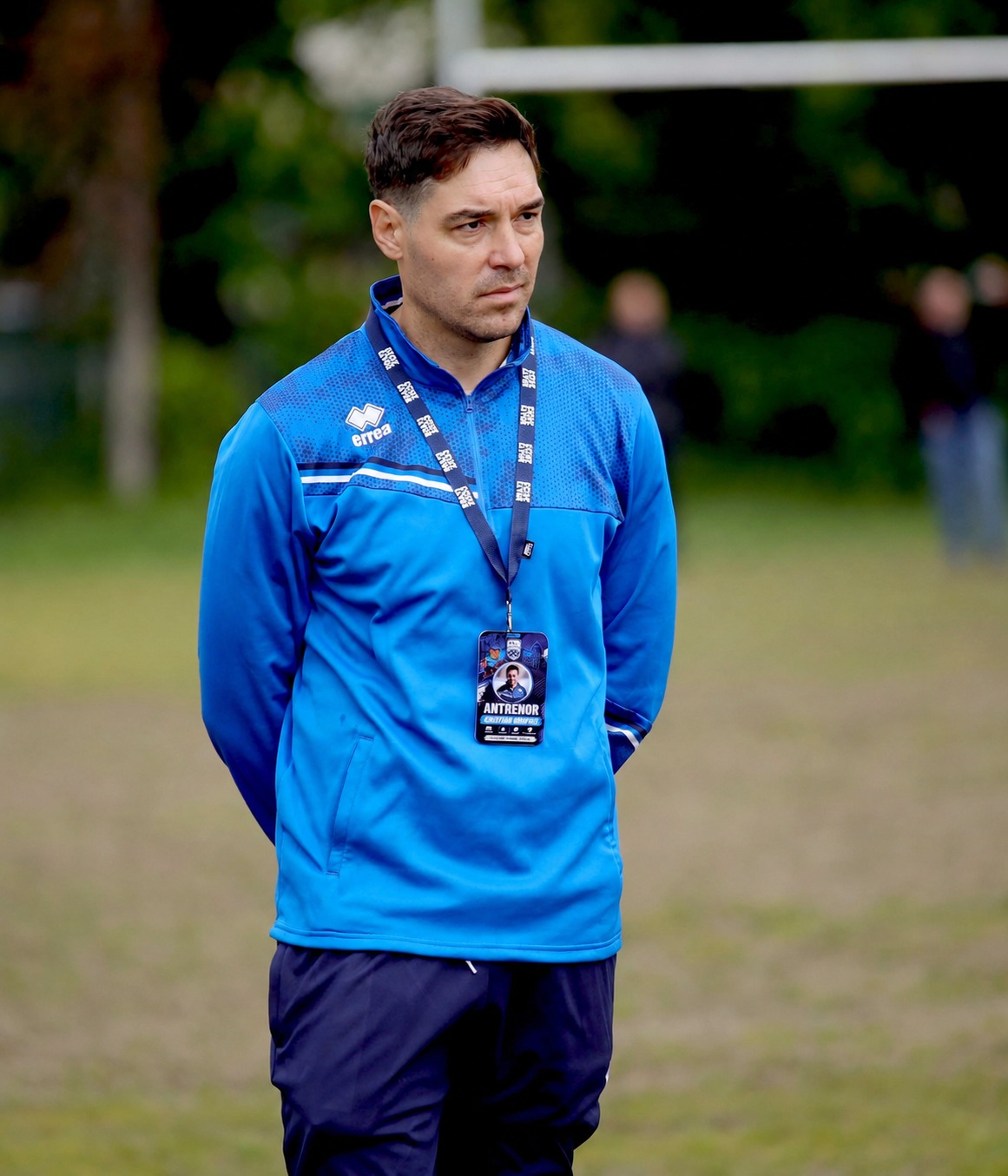 Antrenor de rugby pe marginea terenului, observând jocul și coordonând activitatea echipei în timpul unui antrenament.